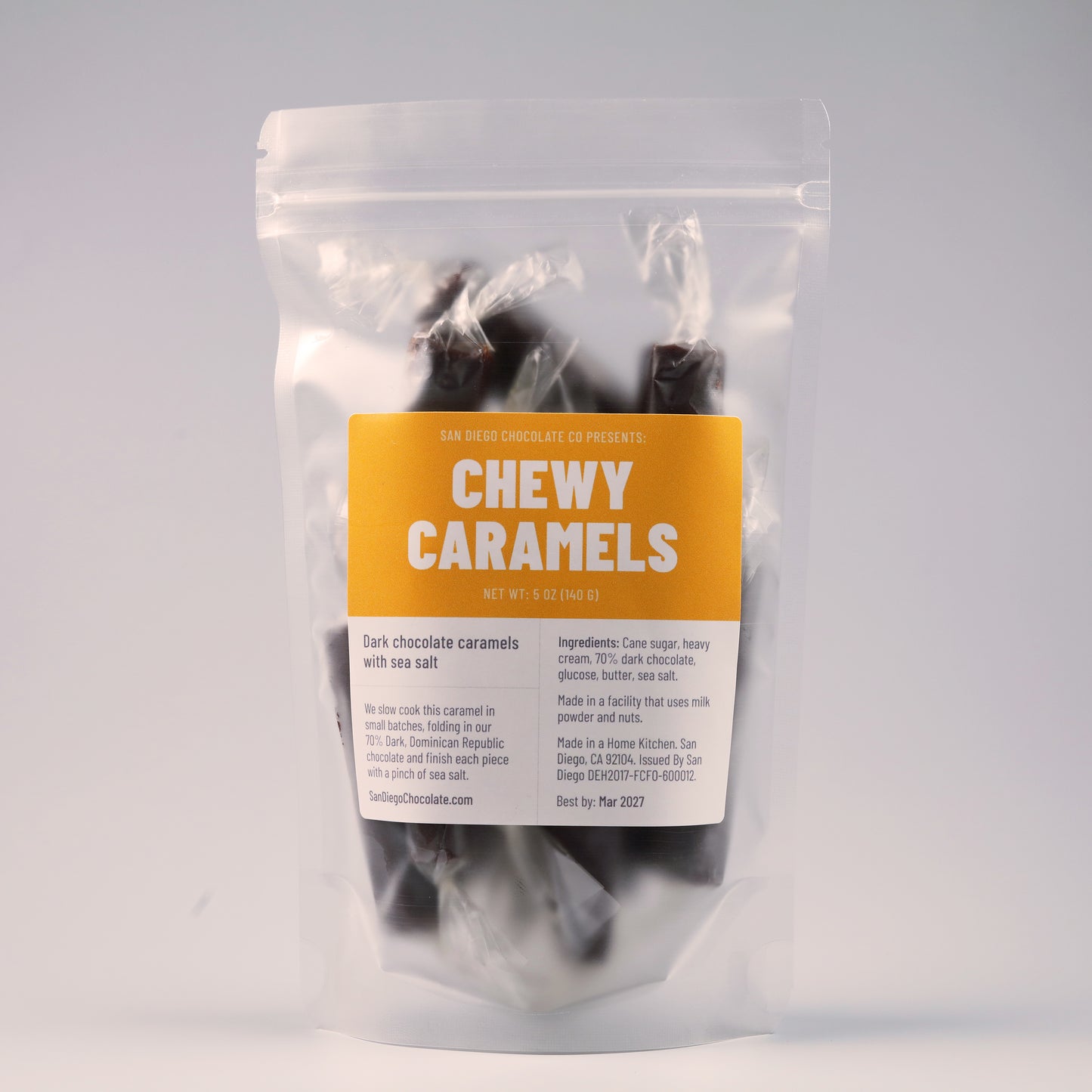 A stand-up pouch of San Diego Chocolate Co. Chewy Caramels, featuring dark chocolate caramels visible through the clear packaging and a bright orange and white label.