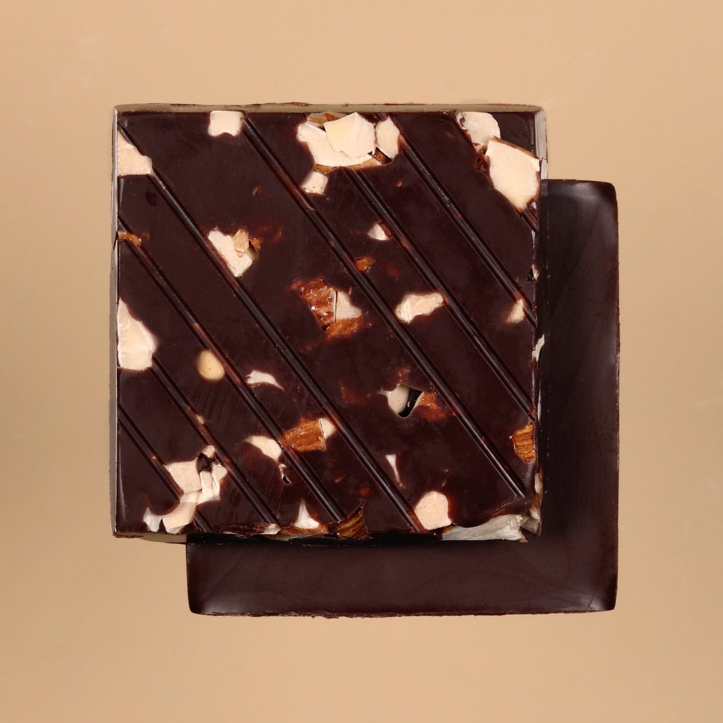 Square piece of chocolate dessert with almond specks on a beige background