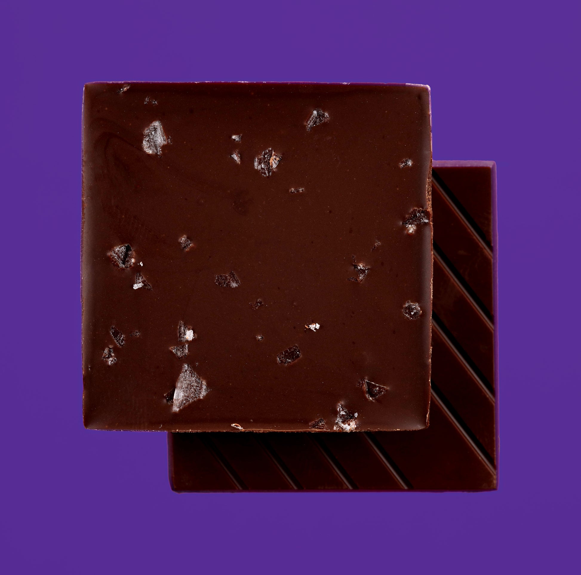 Dark chocolate bar with visible salt pieces on a purple background