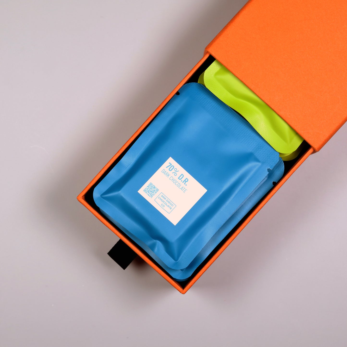 Blue and green chocolate sachets in an orange box on a gray background