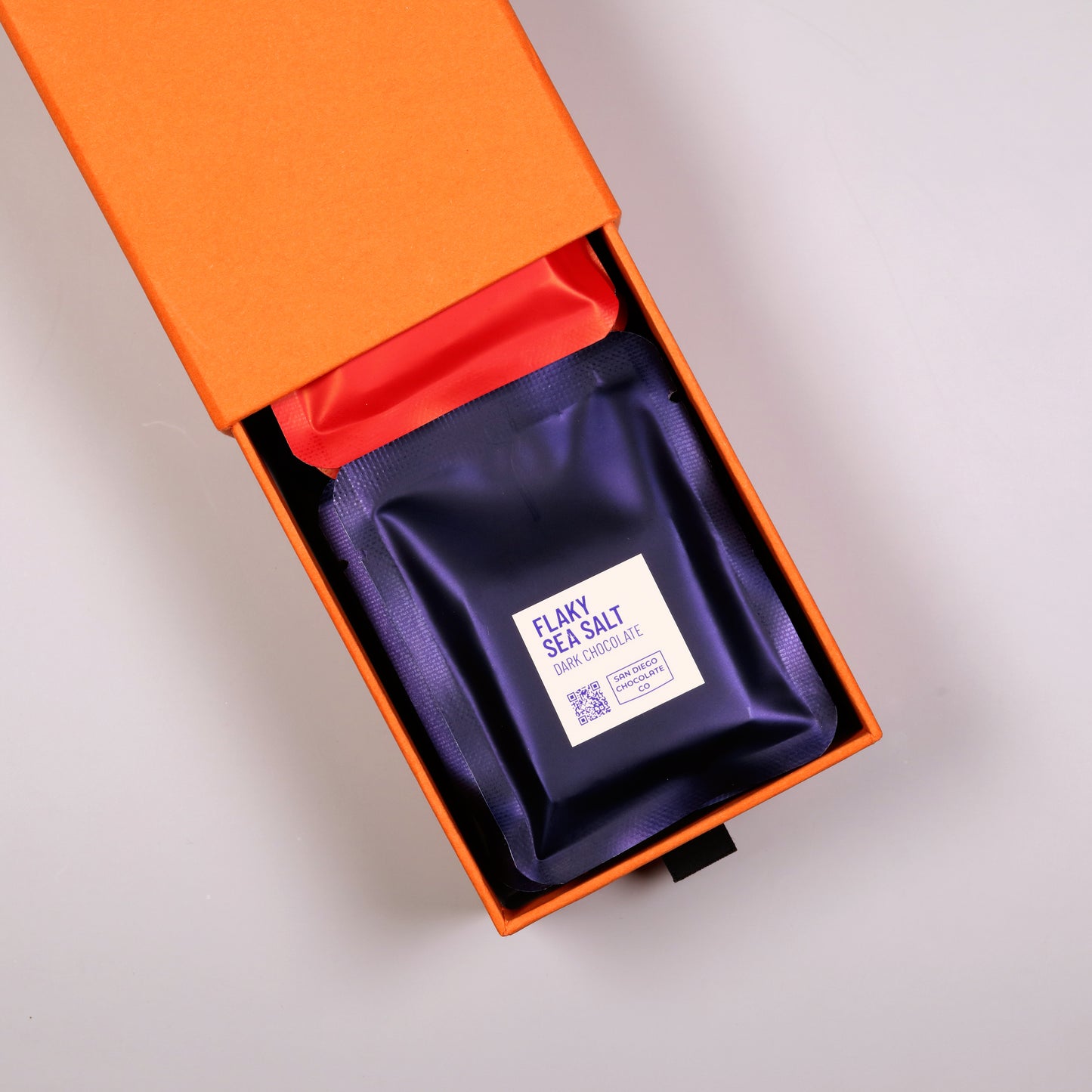 Purple bag of flaky sea salt in an orange box on a light gray background