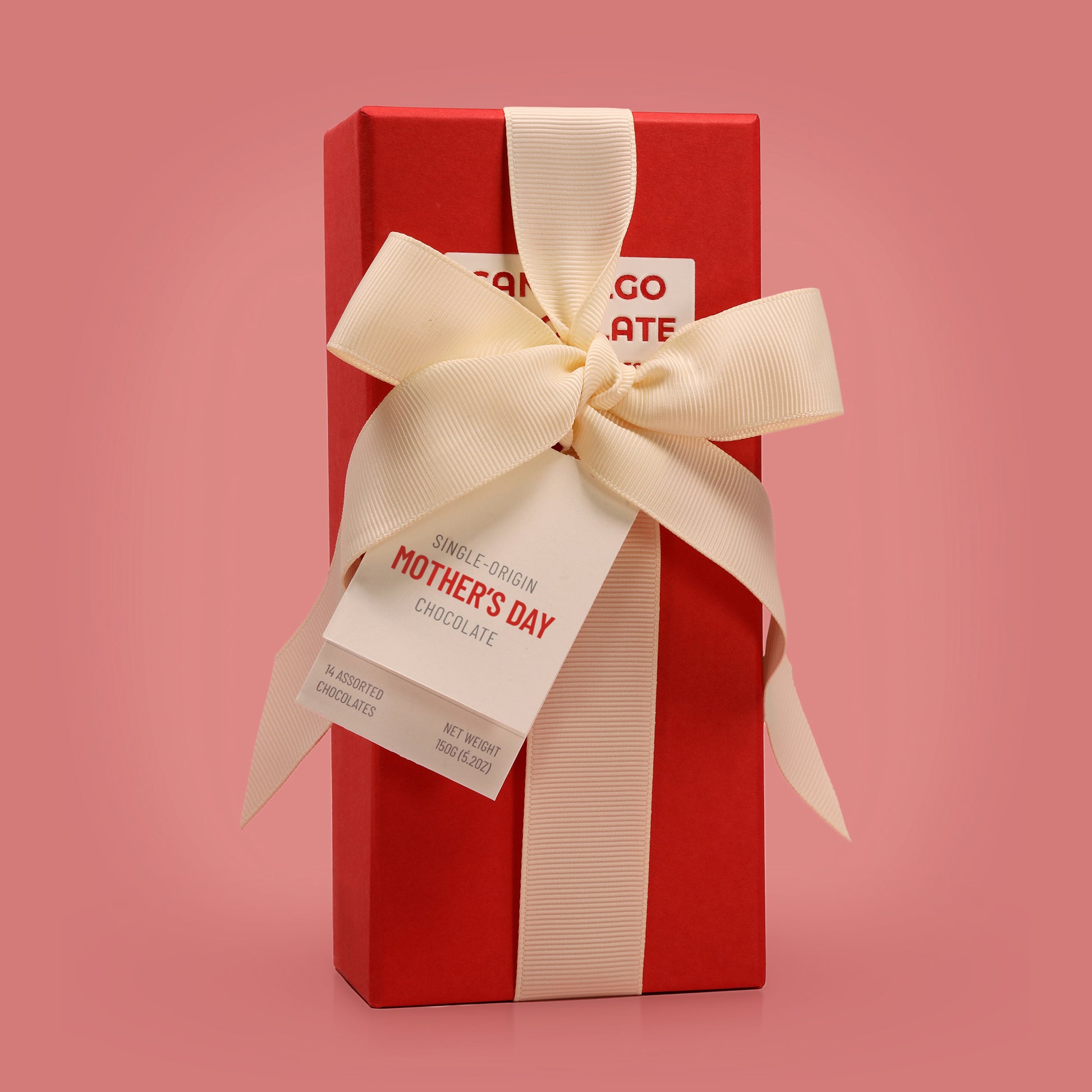 Red gift box with a cream ribbon and 'Mother's Day' tag on a pink background