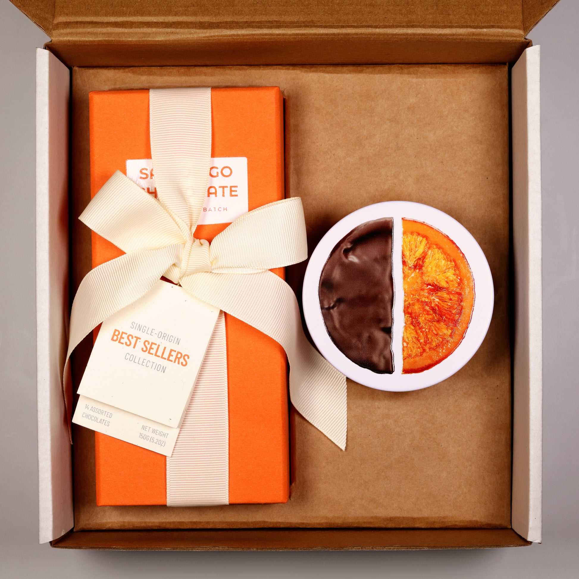 Gift box with an orange and white striped design, a white bow, and a half-chocolate, half-plain cookie in a small white bowl.